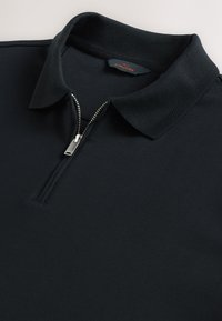 Zwart poloshirt met een rits bij de hals, korte mouwen en een getextureerde kraag. De stof lijkt glad en lichtgewicht. Nette stikdetails.
