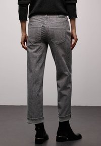 Grå denimjeans med et tekstureret ormmønster, der har opkrogede manchetter, en mellemhøj talje og baglommer. Sorte ankelstøvler bæres.