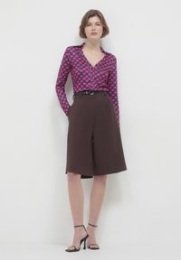 Long-sleeved blouse with pink polka dots on a blue background, paired with brown high-waisted, wide-leg shorts. Black belt and strappy heels.
