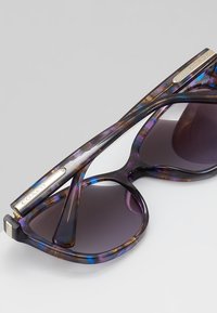 Ochelari de soare tortoise violet cu o ramă groasă, lentile întunecate cu gradient și accente metalice pe temple. Branding Coach vizibil.