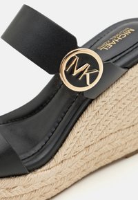 Sandale negre cu toc wedge, având un accent cu logo circular de nuanță aurie, superior din piele și o talpă intermediară din jute țesut cu detalii texturate.