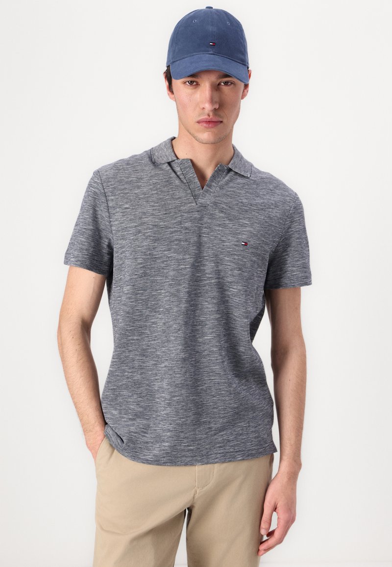 Polo gris de manga corta con un acabado texturizado y un cuello con solapa, combinado con una gorra azul marino que presenta un pequeño detalle de logo.