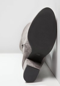 Stivale alla caviglia in suede grigio con tacco quadrato, dotato di una suola in gomma nera testurizzata e un logo discreto sul fondo.