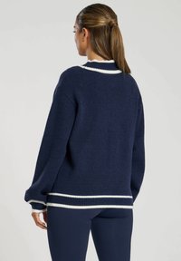 Maglione a maglia navy con vestibilità comoda, caratterizzato da accenti a righe bianche sul colletto e sull'orlo. Tessuto morbido con maniche lunghe e bordi a coste.