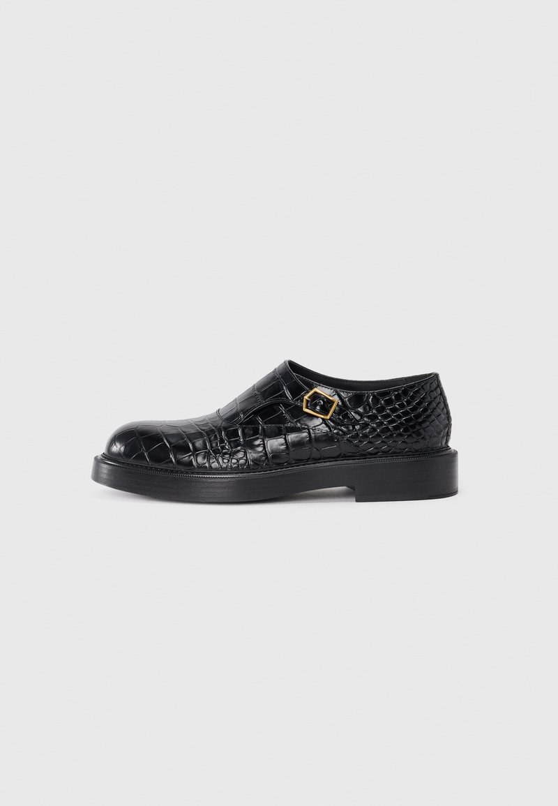 Chaussure en cuir noir avec texture gaufrée crocodile, bout rond, semelle en caoutchouc plate et détail de boucle carrée en ton doré sur le côté.