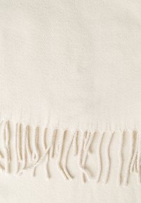 Tissu tissé de couleur crème avec une texture douce et des franges espacées régulièrement le long du bord inférieur.