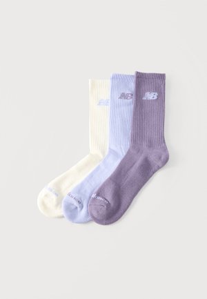 Drei New Balance Socken in Weiß, Hellblau und Lila, überlappend auf einem einfarbigen hellen Hintergrund angeordnet.