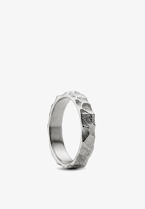 Sølvring med hamret, teksturert overflate og uregelmessige kanter, stående oppreist på en hvit bakgrunn.