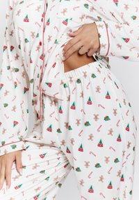Witte pyjama set met een feestelijk patroon van peperkoekmannetjes, kerstbomen, snoepstokken en cadeautjes, met rode bies en een elastische taille.