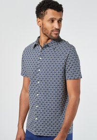 Camicetta a maniche corte di colore blu navy con un motivo geometrico bianco. Presenta una chiusura con bottoni sul davanti e un colletto classico. Tessuto leggero.