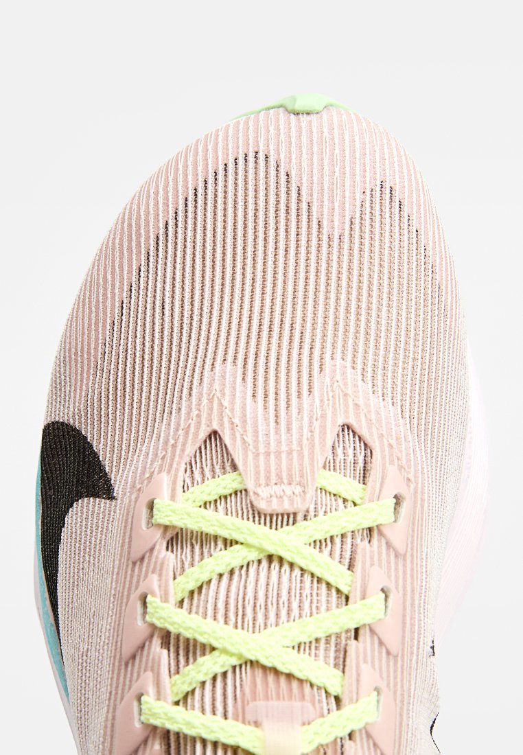 Zapatilla deportiva rosa claro con parte superior de malla texturizada, cordones verde neón y logo negro. Cuenta con un diseño de puntera curva y ojales reforzados.