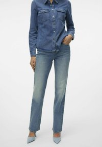 Jeanskjorte med knappelukking, to brystlommer; kombinert med falmede blå jeans og lyseblå spisse hæler.