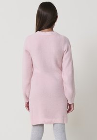 Maglione lungo rosa chiaro con una finitura morbida e testurizzata, dotato di maniche lunghe e orlo a coste. Il design è semplice e privo di decorazioni.