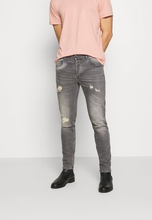 Jeans grises de corte slim con patrones desgastados, que presentan una cintura de altura media, cinco bolsillos y costuras de contraste. Combinados con una camiseta rosa clara.
