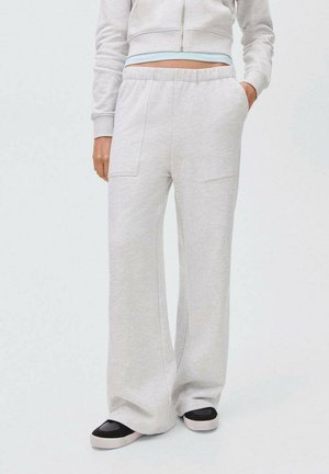 Pantalons de survêtement gris clair avec des jambes larges, une taille élastique et des poches avant. Tissu doux avec une texture lisse, associés à des chaussures noires à enfiler.