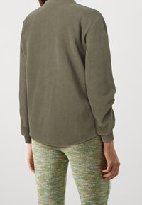 Olivengrøn sweatshirtjakke i fleece med blød tekstur, lange ærmer, rund krave og en afslappet pasform. Kombineret med flerfarvede bukser med tekstur.