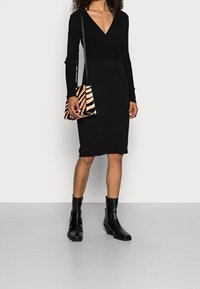 Svart rippad klänning med V-ringning, långa ärmar och en figursydd design. Kombinerad med en randig handväska och svarta ankelstövlar.