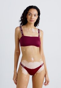 Burgundy swimwear set featuring a crop top with thick straps and adjustable accents, paired with a matching low-rise bikini bottom.