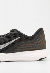 Černá teniska Nike Flex s vrchní částí z materiálu mesh, stříbrným logem Swoosh, barevným duhovým detailem na patě a bílou podrážkou.