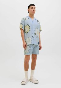 Kortærmet blomster skjorte i lyseblå med store gule og grønne mønstre; matchende shorts i blå; parret med beige slip-on sandaler.