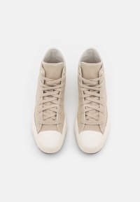 Beige high-top sneakers made of canvas with a textured finish, featuring round laces, a white rubber toe cap, and a contrasting sole.