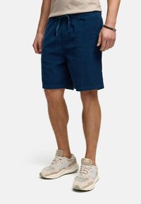 Shorts bleu marine avec une taille élastique et un cordon de serrage, présentant un design décontracté et une texture douce, associés à des baskets beiges.