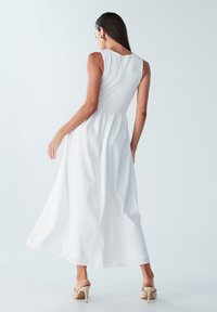 Robe maxi blanche avec un corsage texturé et une jupe fluide. Design sans manches, couture arrière discrète et silhouette décontractée.