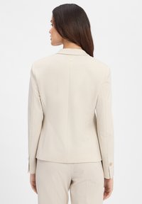 Blazer checkered beige con un fit su misura, colletto a rever, chiusura con singolo bottone e maniche lunghe. Il tessuto testurizzato aggiunge un dettaglio sottile.