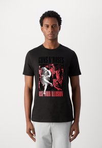 Black cotton t-shirt featuring a graphic print with red and white elements, text "GUNS N' ROSES" and "USE YOUR ILLUSION," short sleeves, crew neck.