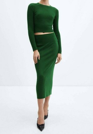 Ensemble à deux pièces en tricot côtelé vert comprenant un haut court à manches longues et une jupe midi, associé à des escarpins noirs à bout pointu.