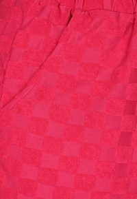 Červená texturovaná látka s kostkovaným vzorem, který obsahuje střídající se hladké a froté čtverce, vytvářející hloubku a kontrast.