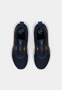 Sötétkék sportcipők narancssárga díszítéssel, hálós anyagból, kerek orral, párnázott szegéllyel és fehér, texturált mintázatú talppal.