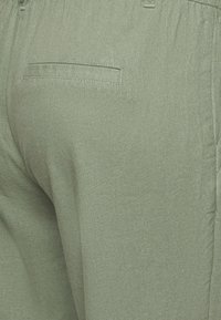 Gröna linnebyxor med en texturerad yta, som har en enda bakficka och resårmidja. Färgen är mjuk och dämpad.