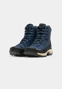 Tumši zili pārgājienu zābaki ar augstu potītes atbalstu, teksturētu augšdaļu, melniem gumijas zoliem un gludām šņorēm ar pelēkiem akcentiem. Dizains uzsver izturību.