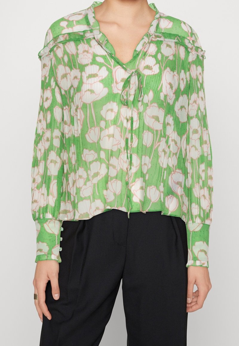 Groene blouse met bloemenpatroon van doorschijnende, geplooide stof. Heeft een V-hals, knoopmanschetten en een strikdetail bij de halslijn.