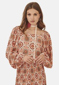 Vestido de manga larga, con cuello descubierto en color coral y estampados florales en rojo, blanco y verde. Presenta una cintura fruncida y un detalle de lazo en el cuello.