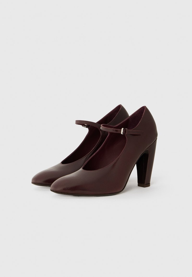 Burgundy höga klackar Mary Jane-skor med rund tå, ankelrem och glansig yta. Har en solid, kraftig klack.