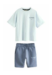 Ljusblå bomullströja med korta ärmar och en logotyp, i kombination med grå bomullsshorts med fickor och elastisk midja.