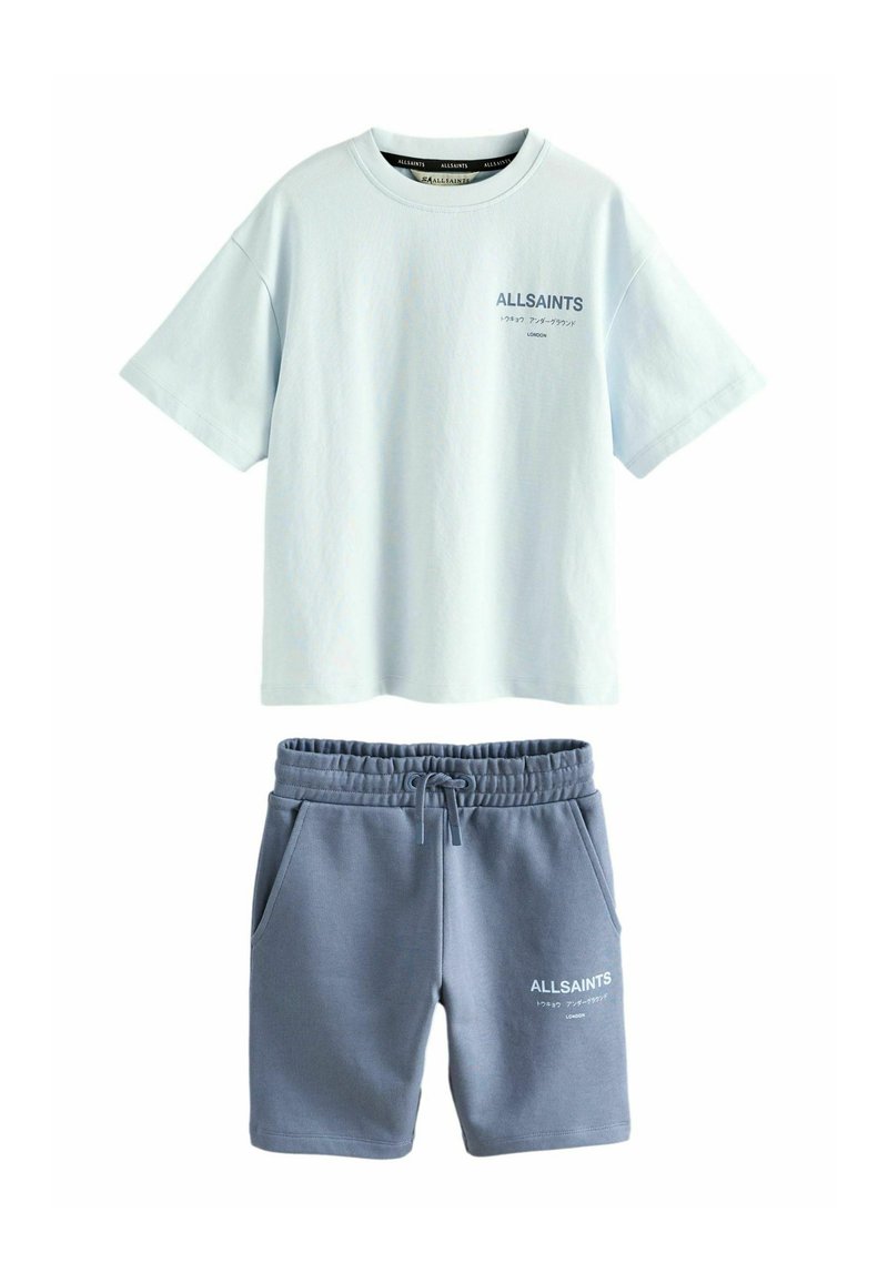Ljusblå bomullströja med korta ärmar och en logotyp, i kombination med grå bomullsshorts med fickor och elastisk midja.