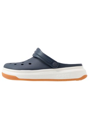 Sabot bleu marine à enfiler avec des trous de ventilation, une bride arrière réglable, une semelle intermédiaire blanche épaisse et une semelle extérieure en caoutchouc orange.