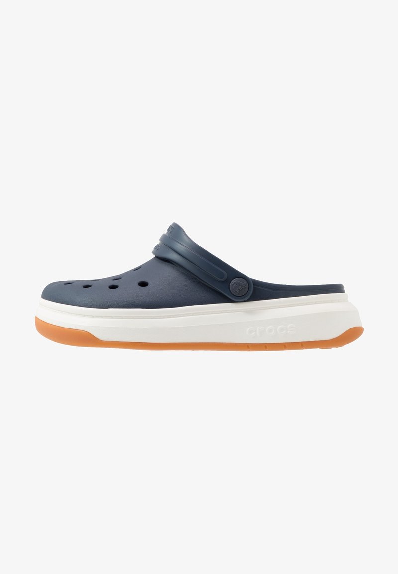Sabot bleu marine à enfiler avec des trous de ventilation, une bride arrière réglable, une semelle intermédiaire blanche épaisse et une semelle extérieure en caoutchouc orange.