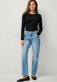 Sort langærmet top, lyseblå lige ben jeans med falmende vask og sorte flade sko. Outfittet understreger en afslappet stil.