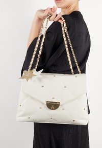 Biały pikowany torebka wykonana z materiału syntetycznego, z złotymi łańcuchami, złotymi elementami metalowymi i akcentami w kształcie gwiazdy. Ozdobiona wstawkami z ćwiekami.
