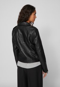 Black leather jacket with a fitted design, featuring a back vent, snap buttons, and zippered cuffs over a gray layered top.