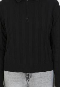 Pullover nero a coste con colletto a mezza zip, caratterizzato da un design a maglia testurizzata. L'orlo inferiore è a coste per una maggiore struttura.