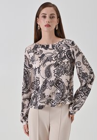 Blusa fluida a maniche lunghe di colore rosa chiaro con una trama paisley nera. Presenta un collo a barchetta e una vestibilità leggermente ampia. Il materiale sembra morbido e setoso.