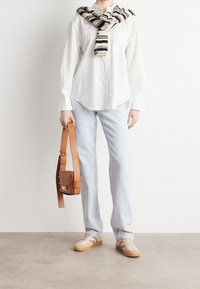 Vit långärmad skjorta, ljusblå jeans, beige sneakers med bruna accenter, brun läderväska med långrem, stickad svart och krämfärgad halsduk.