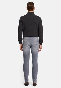 Pullover grigio scuro con colletto alto, abbinato a jeans slim-fit grigio chiaro. Cuciture notevoli sui jeans, e scarpe marroni completano il look.