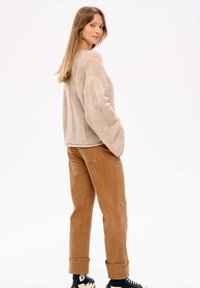 Beige gestrickter Pullover mit weiten Ärmeln, kombiniert mit braunen Baumwollhosen, die an den Bündchen hochgerollt sind, und schwarzen Sneakers. Einfaches und lässiges Design.