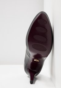 Czarna skórzana szpilka z wąskim noskiem, gładką cholewką i bordową podeszwą z teksturowanymi wzorami antypoślizgowymi.